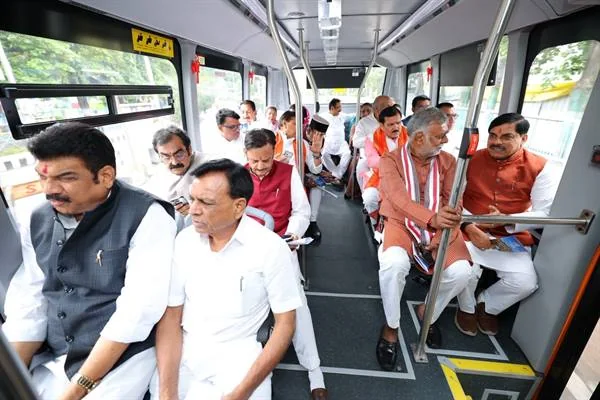 इलेक्ट्रिक बस के अंदर मुख्यमंत्री और मंत्री सीटों पर बैठे हैं, खिड़की के बाहर पेड़ दिख रहे हैं